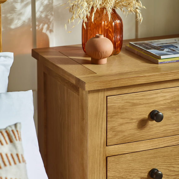 Wooden nightstand with decorative items including a vase and books, in a bedroom setting.