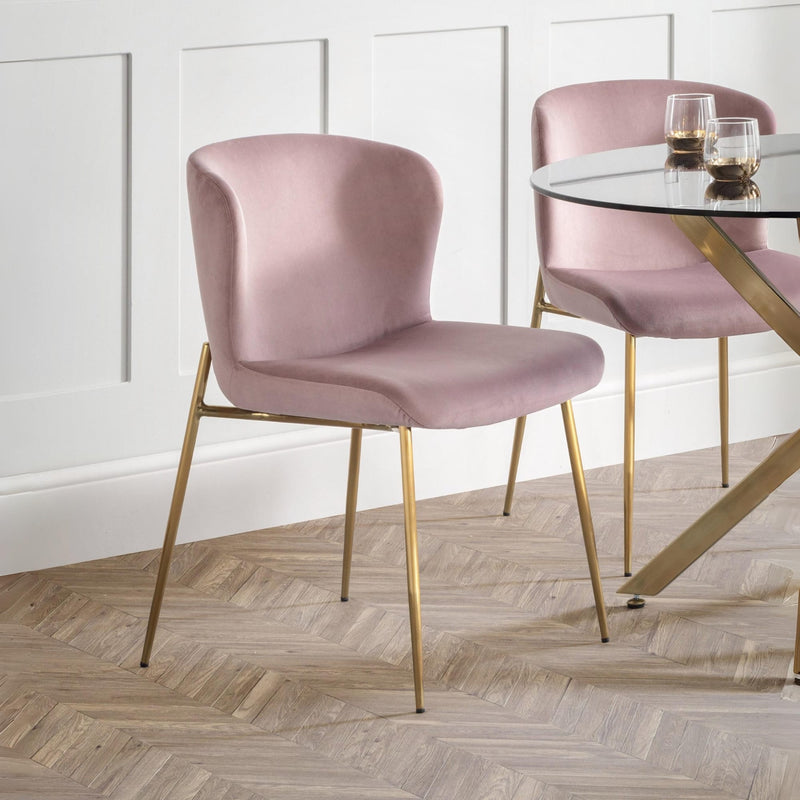 Pink chairs with gold legs around a glass-top dining table on a wooden floor.