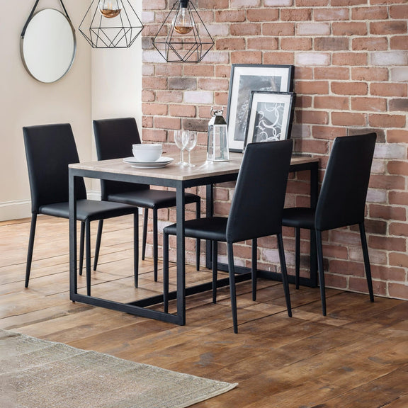Dining area with a table and four black chairs against a brick wall.