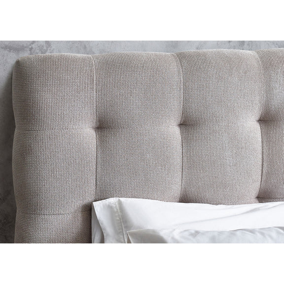 Gray upholstered headboard with tufted details against a neutral wall.