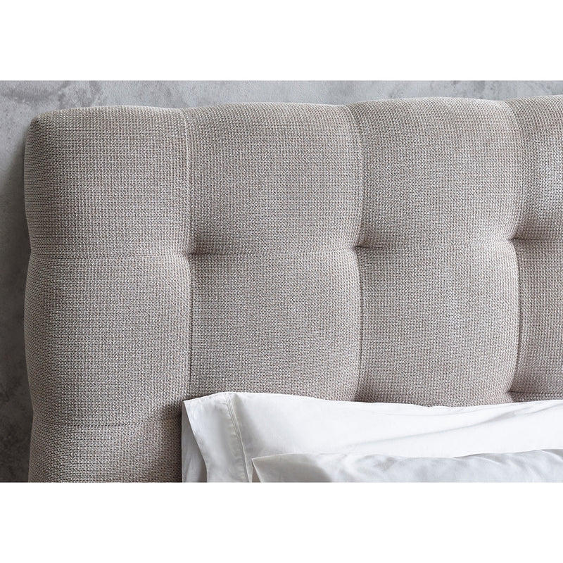 Gray upholstered headboard with tufted details against a neutral wall.