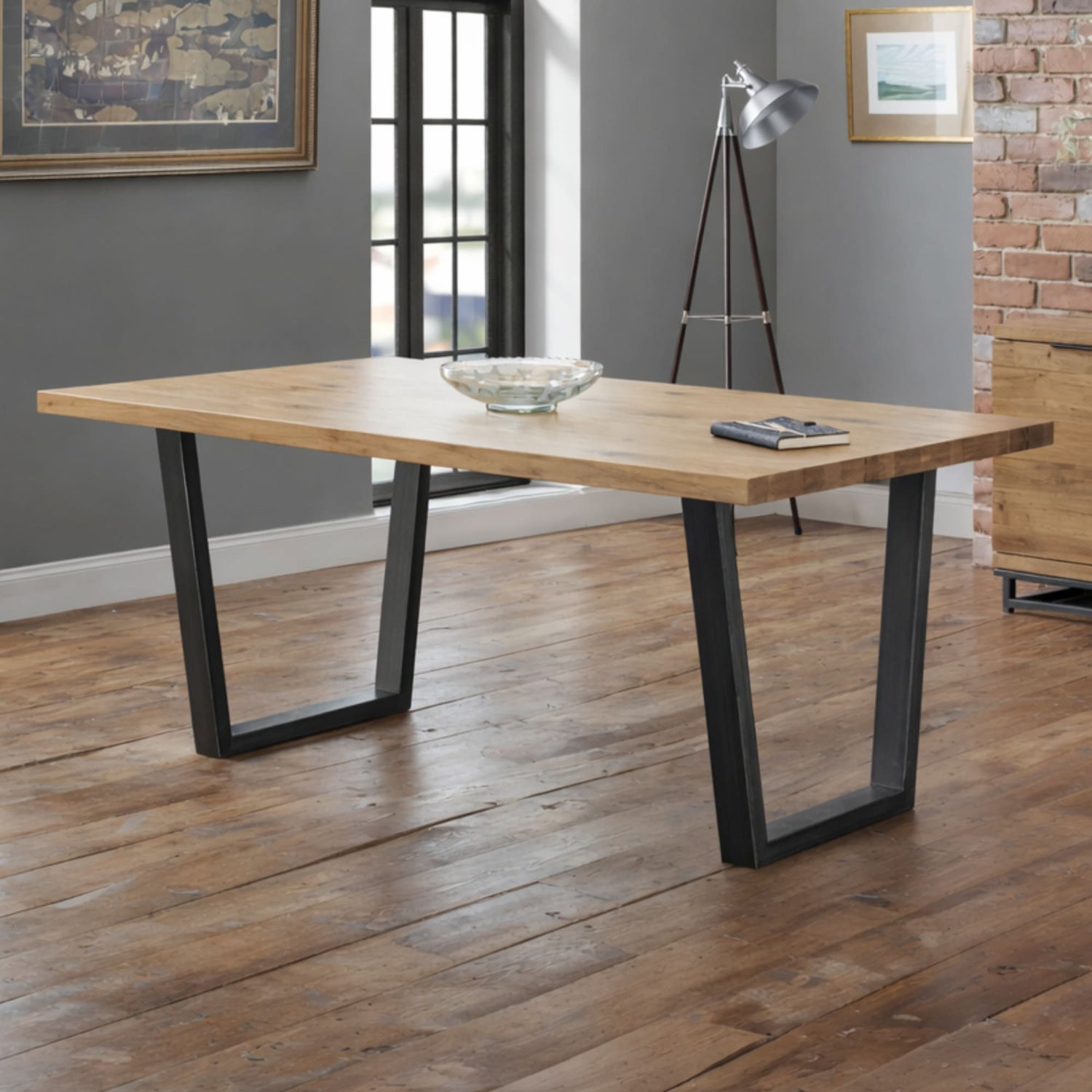 Wooden dining table with black metal legs in a room with gray walls and a brick wall.