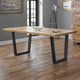 Wooden dining table with black metal legs in a room with gray walls and a brick wall.