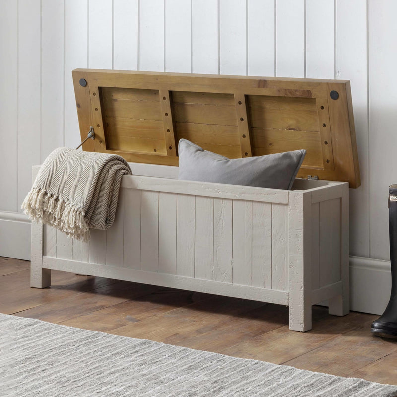 Wooden storage bench with a blanket and pillow against a white paneled wall.
