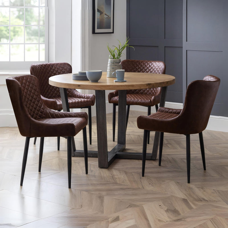 Dining room with round wooden table and four brown chairs on a herringbone floor.