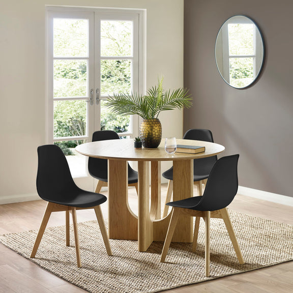 Dining room with a round wooden table and black chairs, featuring a plant and a book on the table.