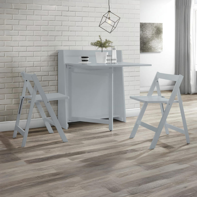 White folding table with two matching chairs on a wooden floor against a white brick wall.