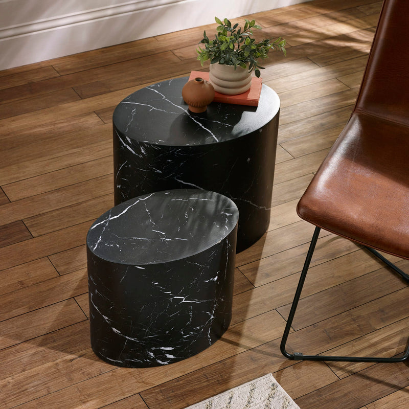 Two black marble side tables on a wooden floor with a chair and plant in the background.