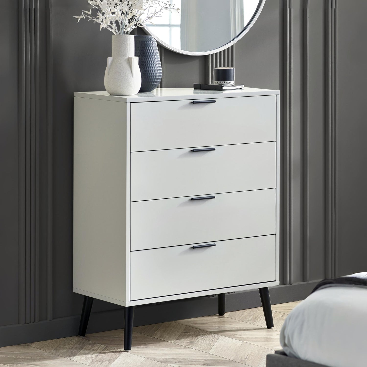 White dresser with black legs against a gray wall in a bedroom setting.