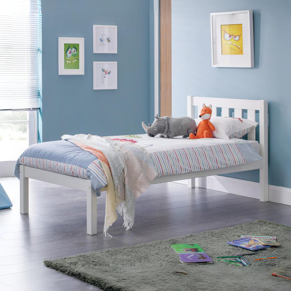 Children's bedroom with a white bed, colorful bedding, and toys on a blue wall.