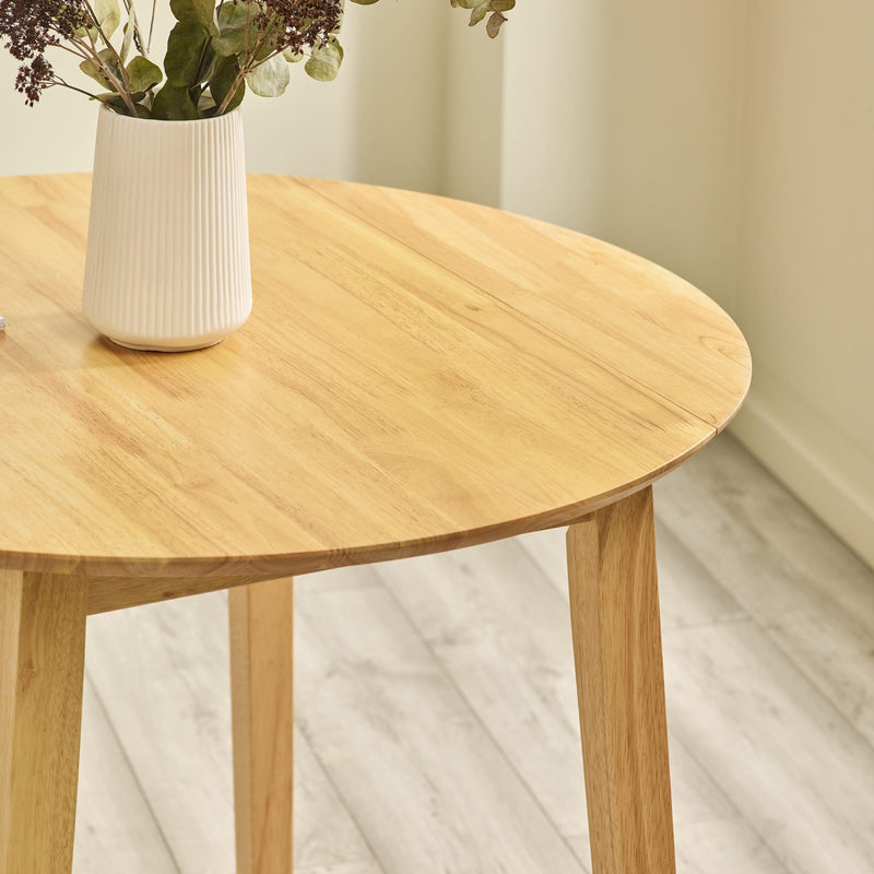 Wooden table with a white vase containing greenery on a light wooden floor.