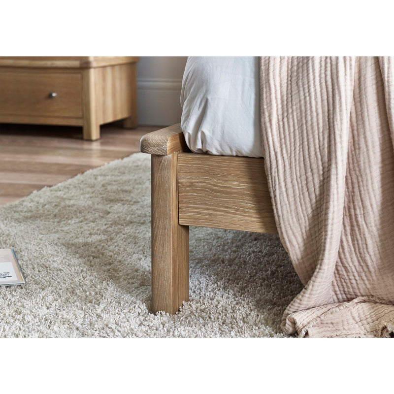 Wooden bed frame with a textured beige blanket on a carpeted floor.