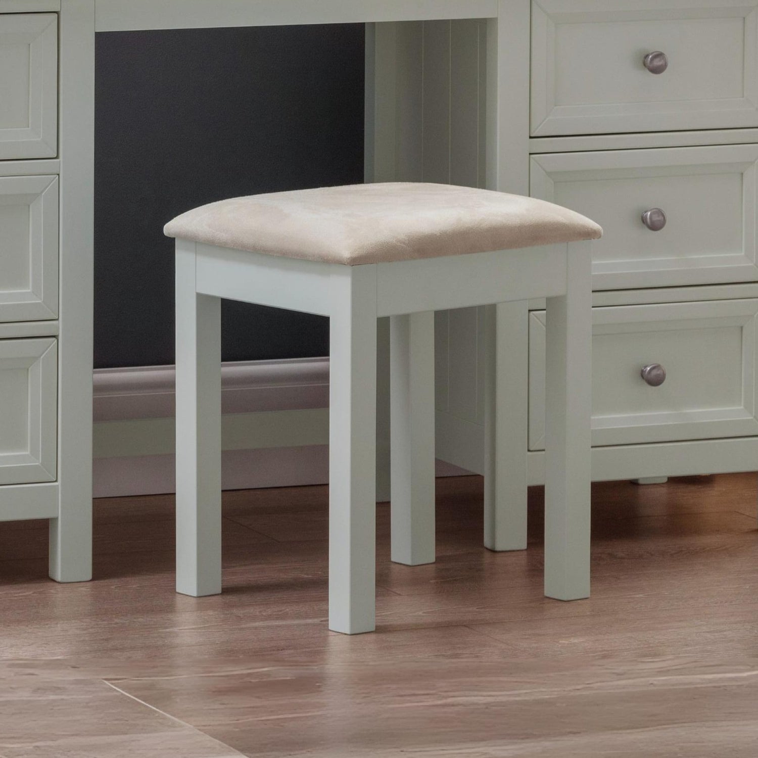 Small stool with a beige cushion in front of a dresser with drawers.