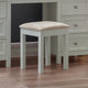 Small stool with a beige cushion in front of a dresser with drawers.