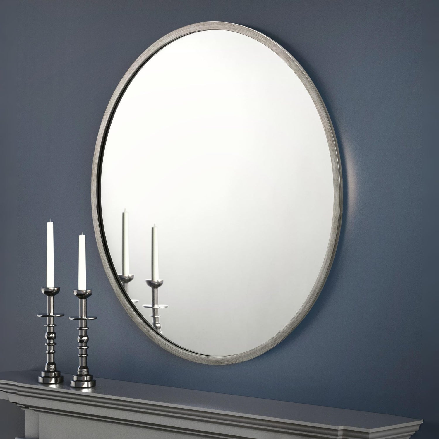 Round mirror on a blue wall with two candlesticks on a mantelpiece.