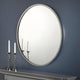 Round mirror on a blue wall with two candlesticks on a mantelpiece.