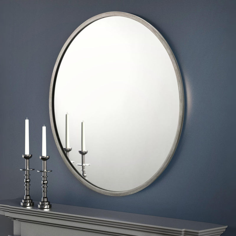 Round mirror on a blue wall with two candlesticks on a mantelpiece.