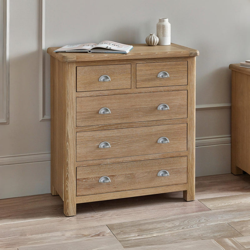 Wooden chest of drawers with four drawers on a wooden floor against a neutral wall.