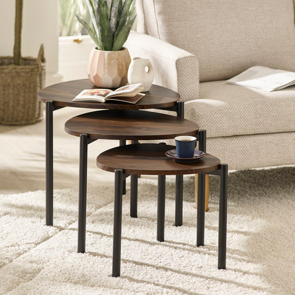 Set of three wooden nesting tables in a living room setting with a cup and book on top.