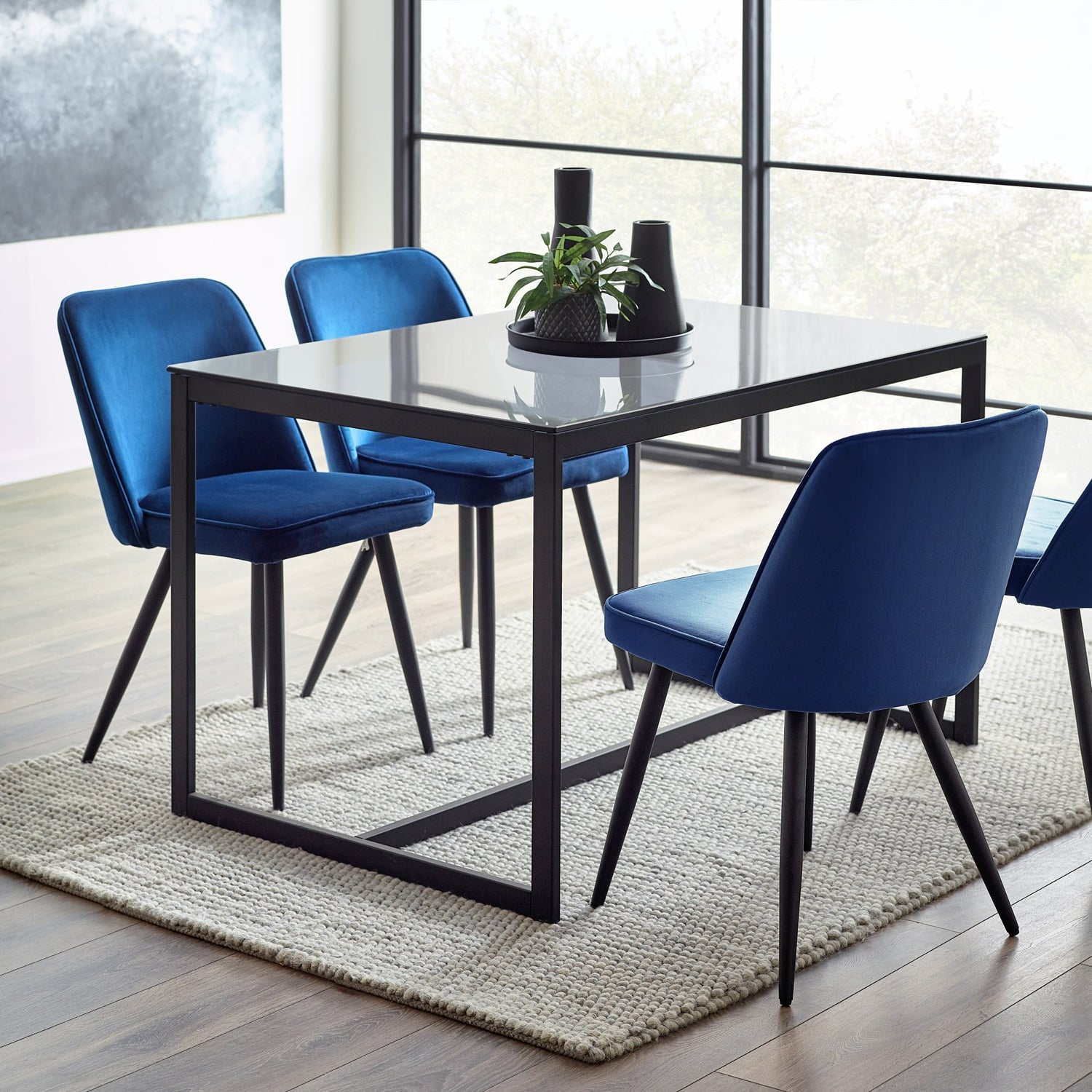 Dining table with four blue chairs in a modern room with large windows.