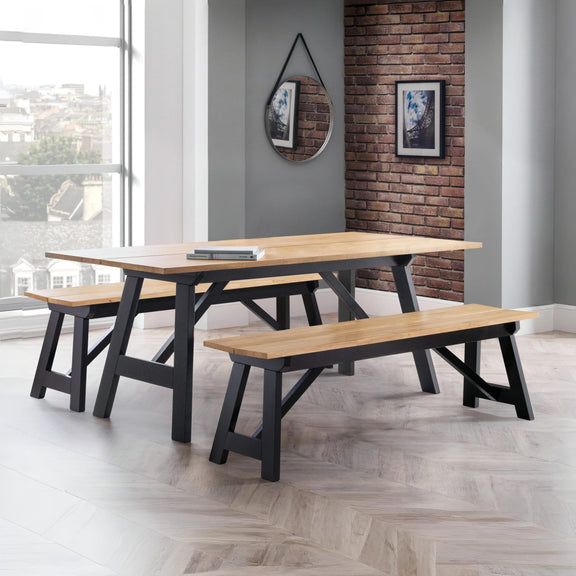 Wooden dining table with benches in a modern room with large windows and brick wall.