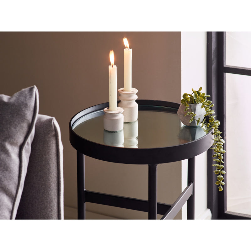 Round black table with white candles and a plant in a room setting