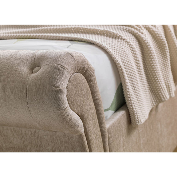 Close-up of a beige upholstered headboard with a textured blanket draped over it.