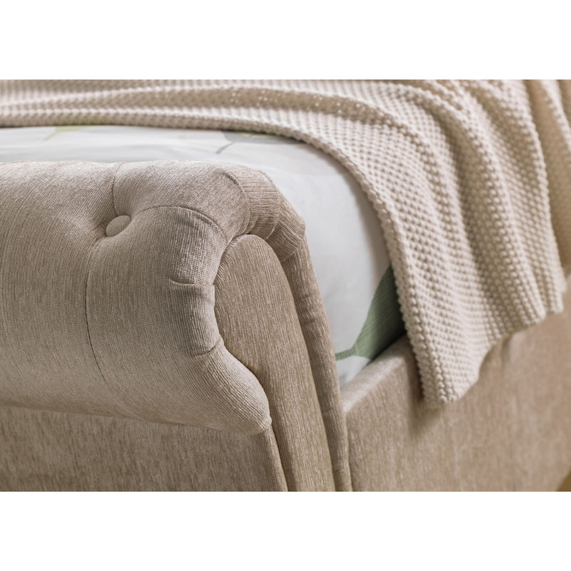 Close-up of a beige upholstered headboard with a textured blanket draped over it.