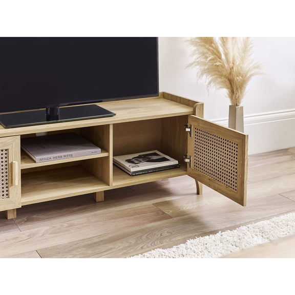 Wooden TV stand with a television on top, books inside, and a vase with plants on a wooden floor.