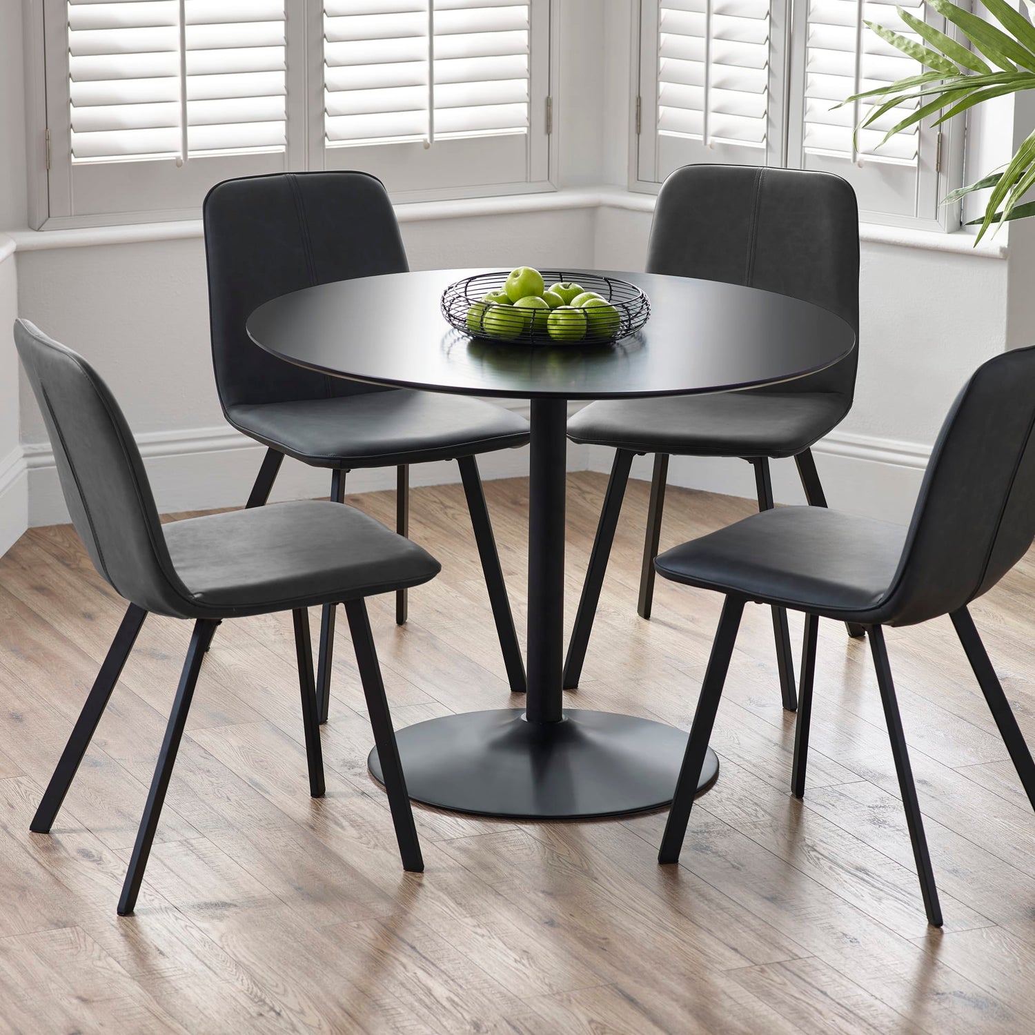 Black round dining table with four matching chairs in a room with large windows.