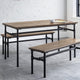 Wooden dining table with benches on a concrete floor against a white brick wall.