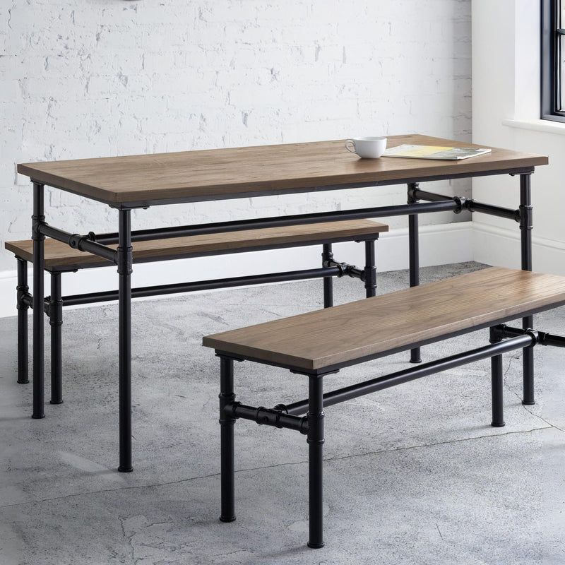 Wooden dining table with benches on a concrete floor against a white brick wall.