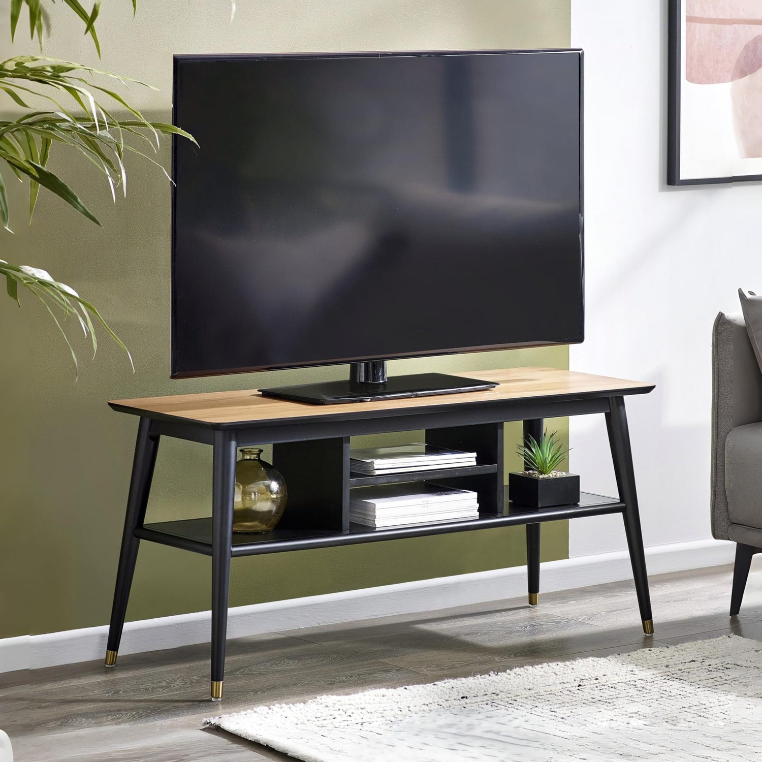 TV on a wooden stand in a living room setting with a plant and sofa.