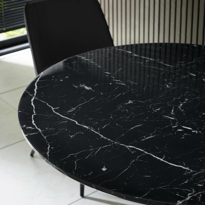 Black marble table with a chair in a room with white tiled floor and black radiator.