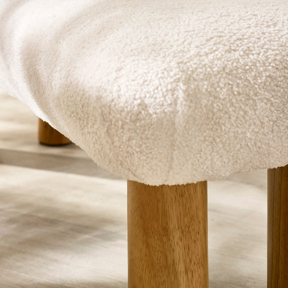 Close-up of a textured white cushioned stool with wooden legs on a light wood floor.