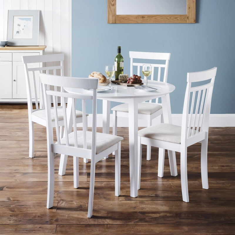 White dining table with four chairs in a room with a blue wall and wooden floor.