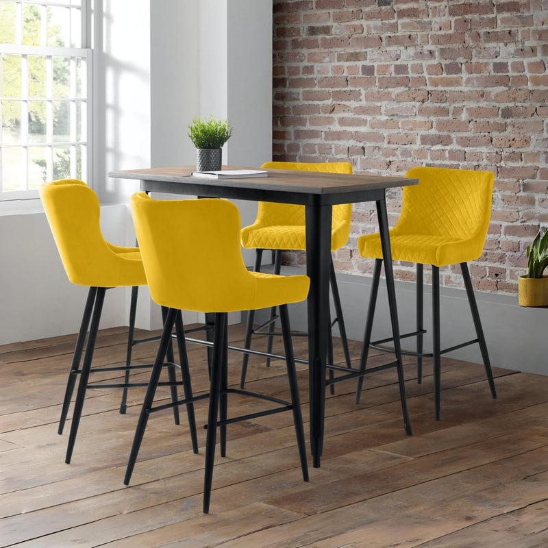 Four yellow bar stools around a black dining table with a brick wall background.