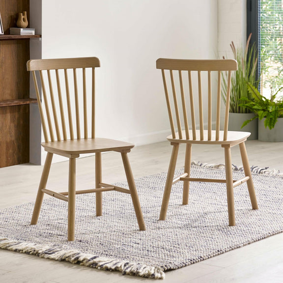 Two wooden chairs on a textured rug with a neutral background