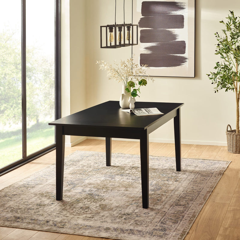 Black dining table in a room with large windows, rug, and decorative elements.