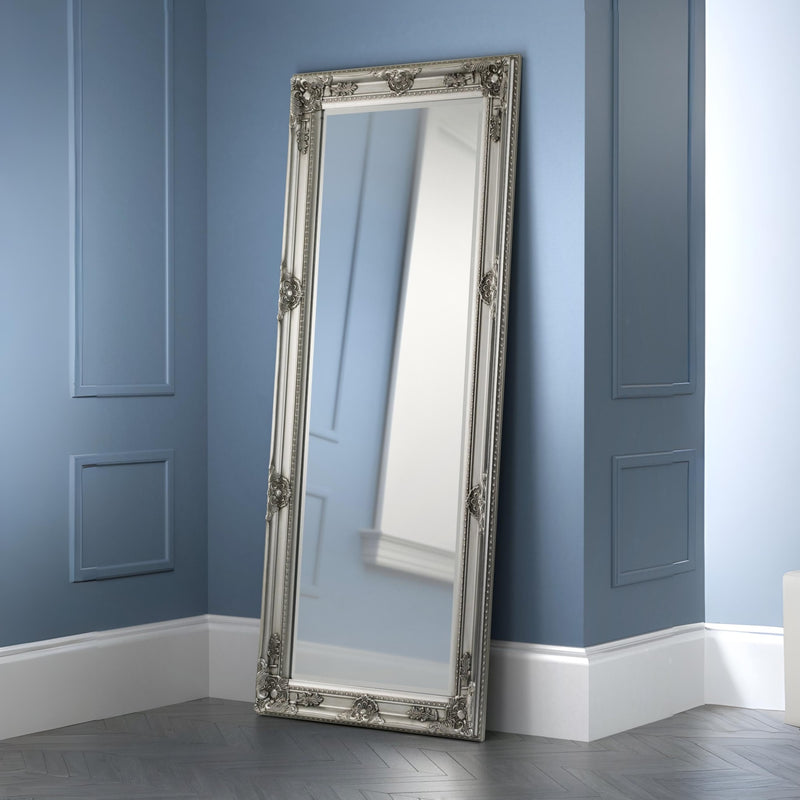 Decorative floor mirror with silver frame against a blue wall