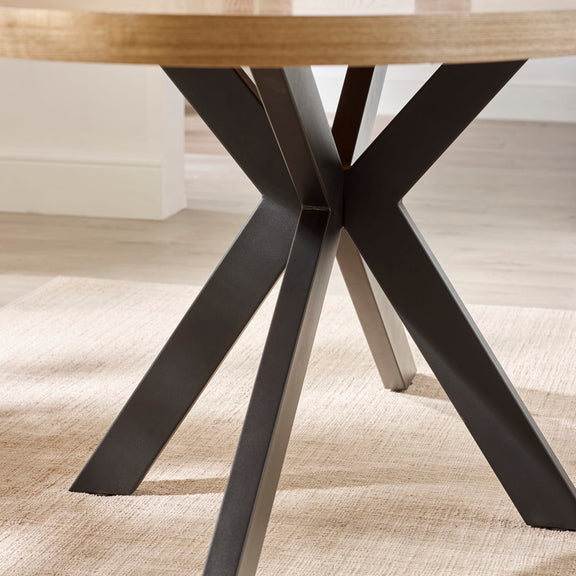 Close-up of a wooden table with a black metal base on a textured floor.