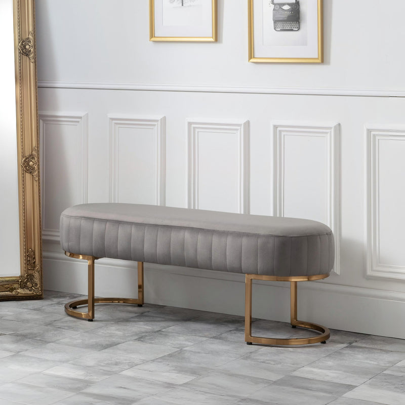 Gray upholstered bench with gold legs in a room with white paneled walls and decorative mirrors.