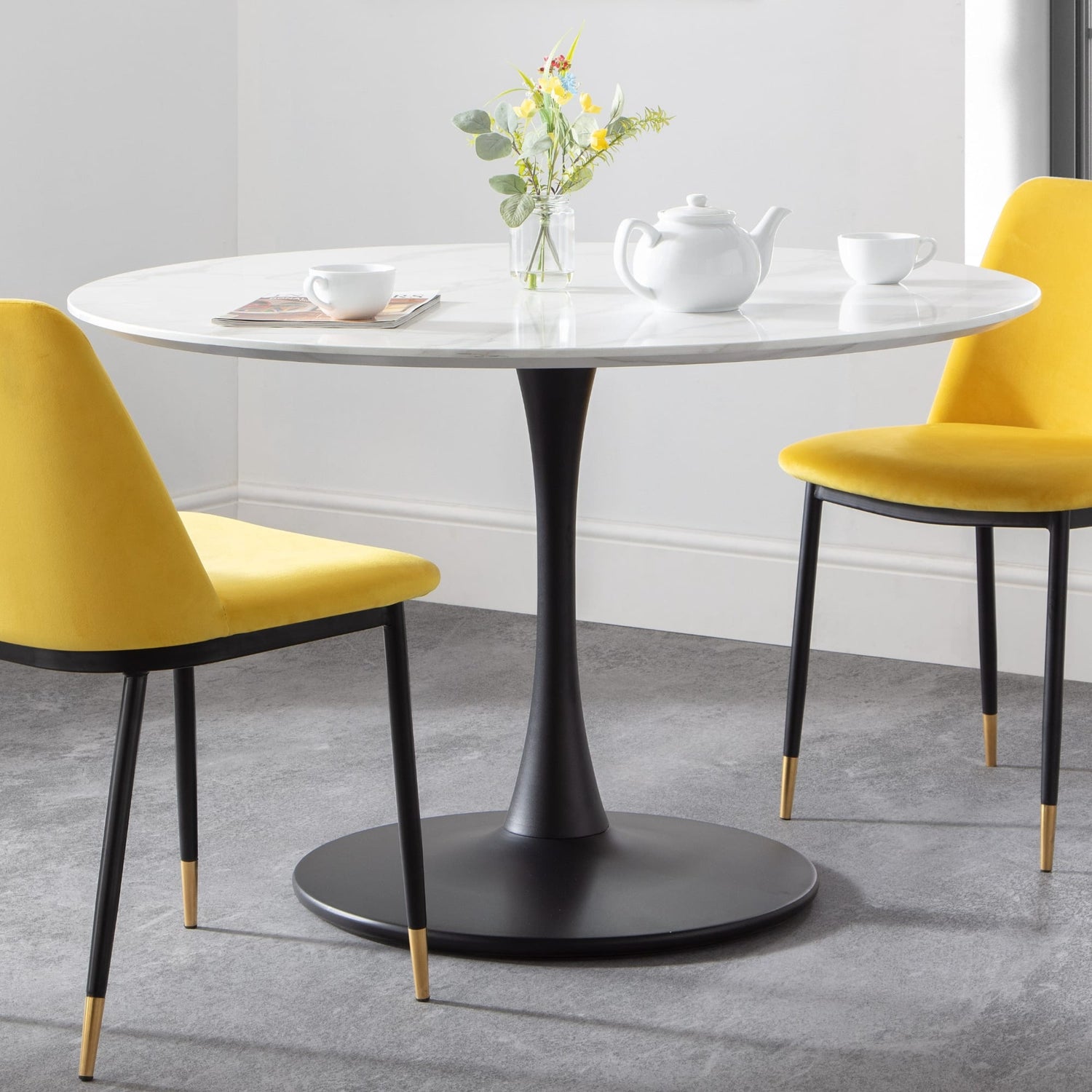 Round dining table with black pedestal base and two yellow chairs in a room.