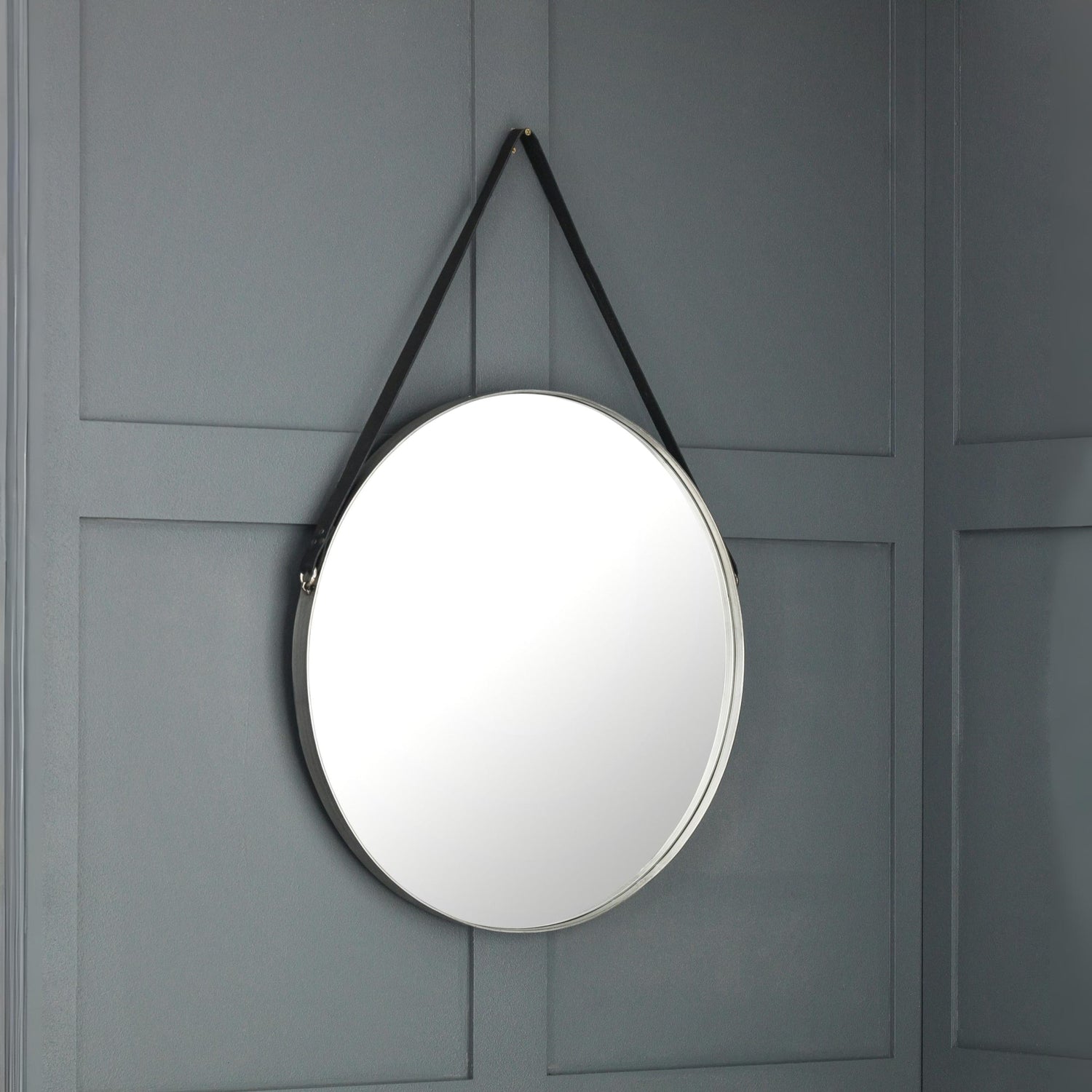 Round mirror with black strap hanging on a gray paneled wall