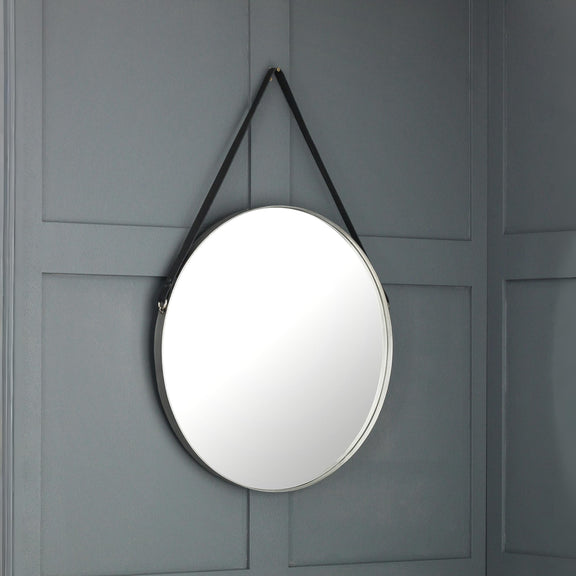 Round mirror with black strap hanging on a gray paneled wall