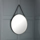 Round mirror with black strap hanging on a gray paneled wall