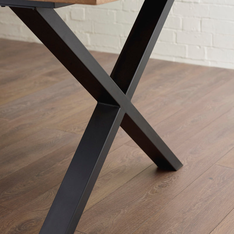 Close-up of a black metal table leg on a wooden floor with a white brick wall in the background.