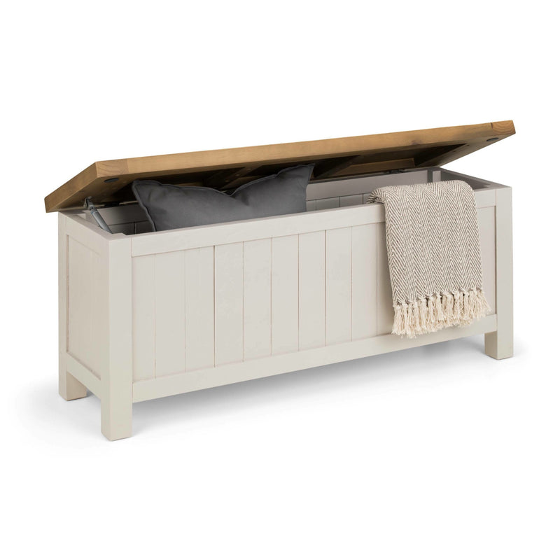 White storage bench with wooden lid containing pillows and a blanket on a white background