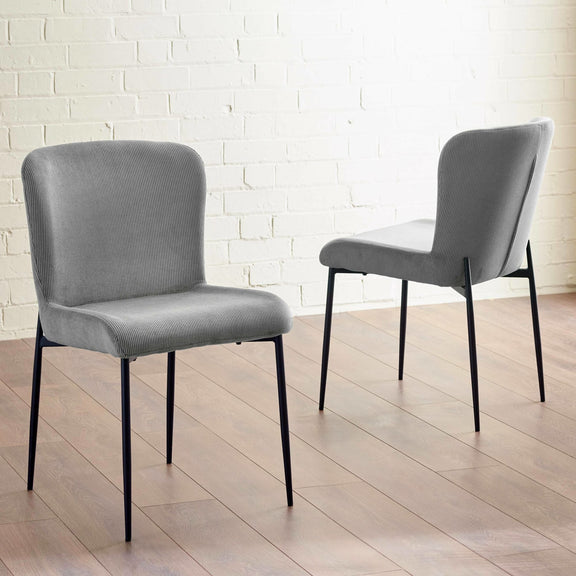 Two gray chairs with black legs on a wooden floor against a white brick wall.
