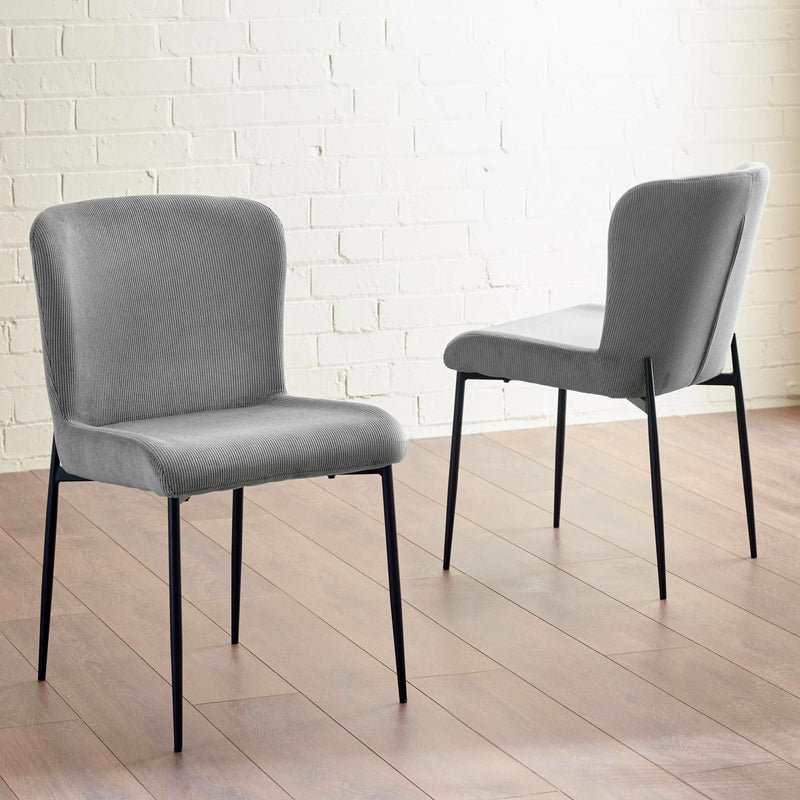 Two gray chairs with black legs on a wooden floor against a white brick wall.